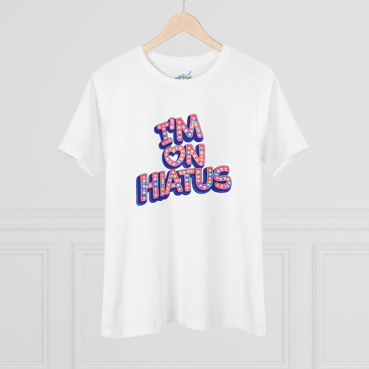 White short-sleeve crewneck graphic t-shirt featuring the "I'm On Hiatus" marquee design, hanging on a wood hanger against a light gray wall